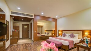 Une chambre d’hôtel avec un grand lit, un coin salon, une télévision et un miroir.