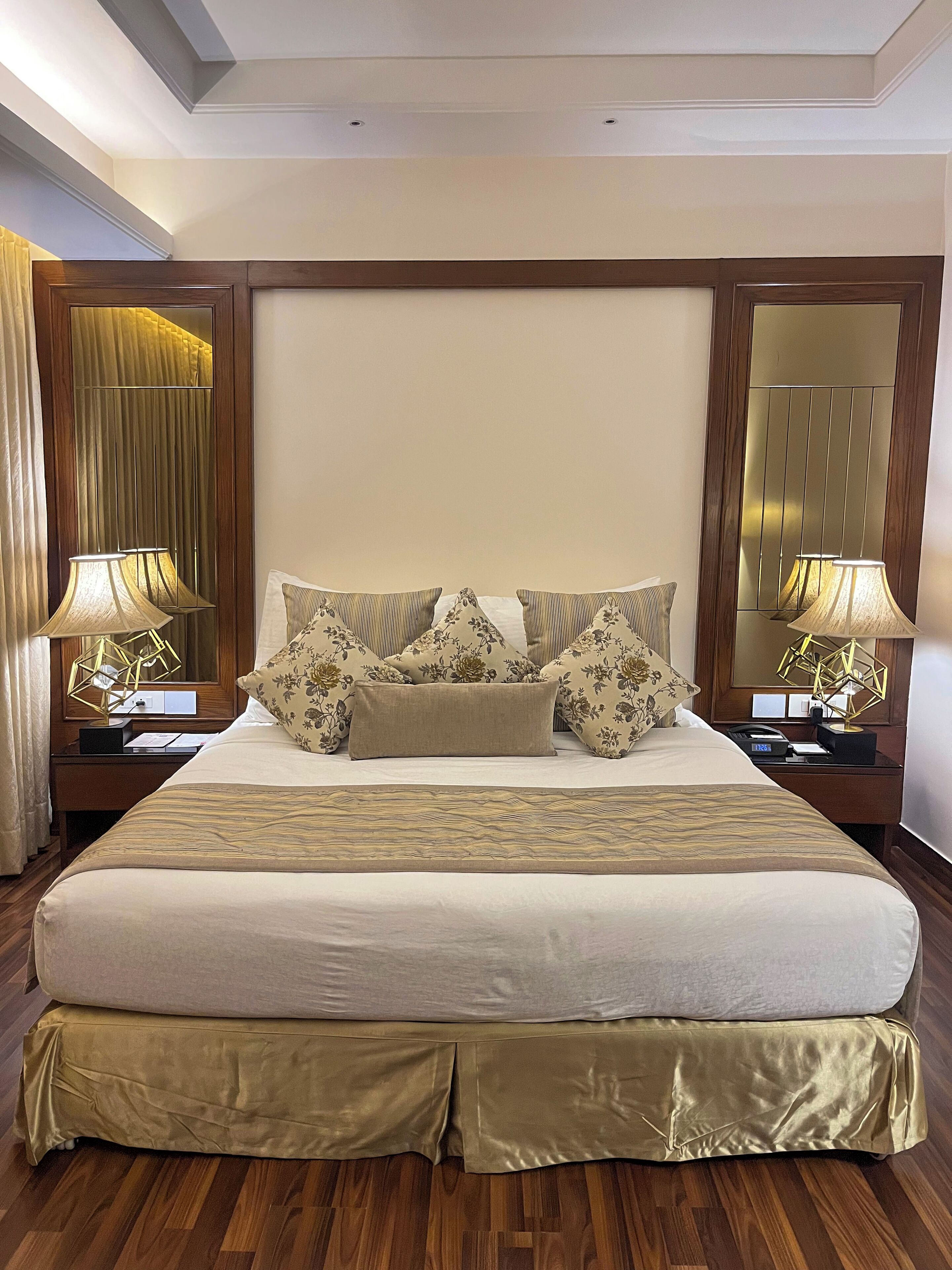 A large bed with a wooden headboard, two bedside tables with lamps, and a mirror on the wall.