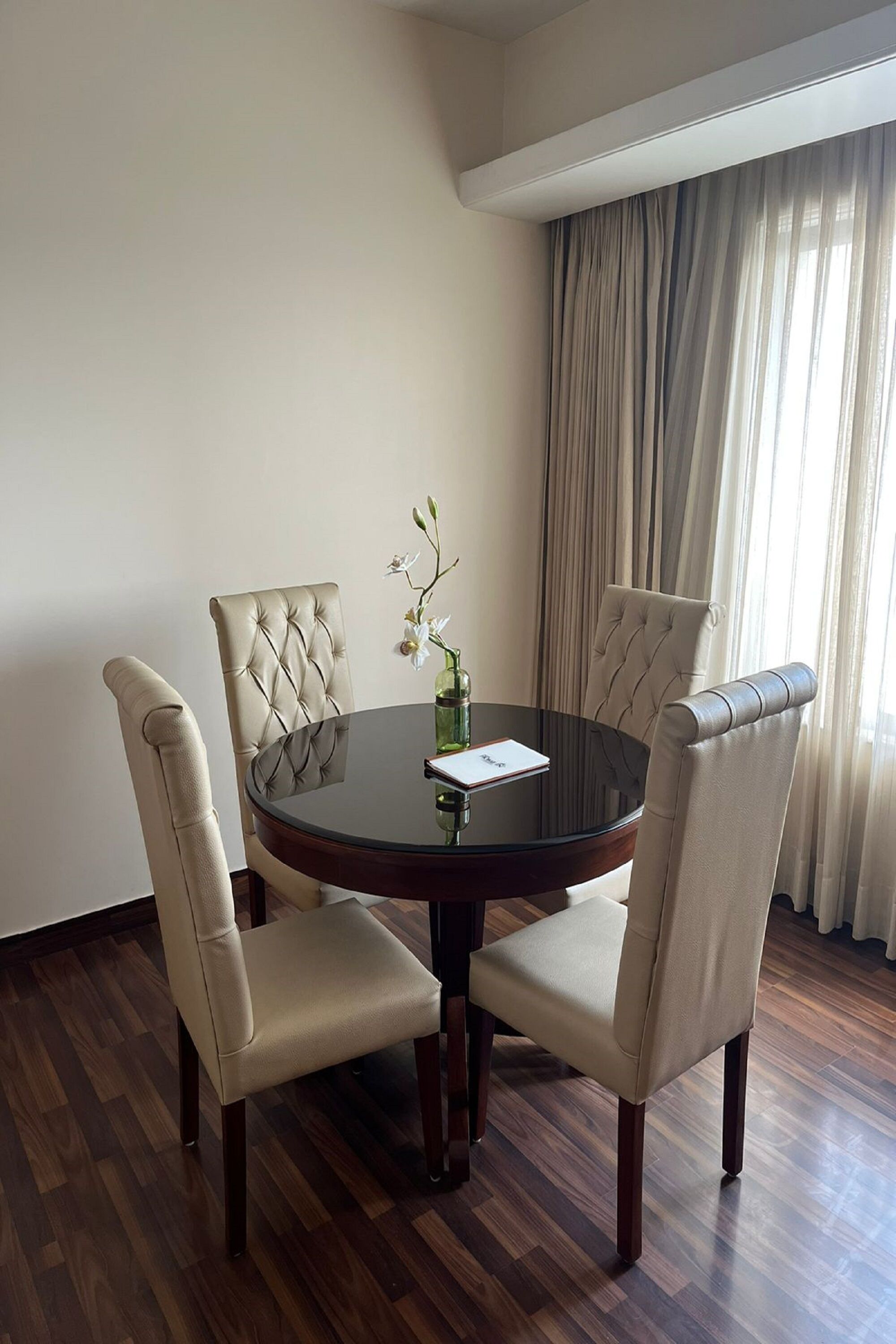 A round dining table with four upholstered chairs, a vase with flowers, and a menu on the table.