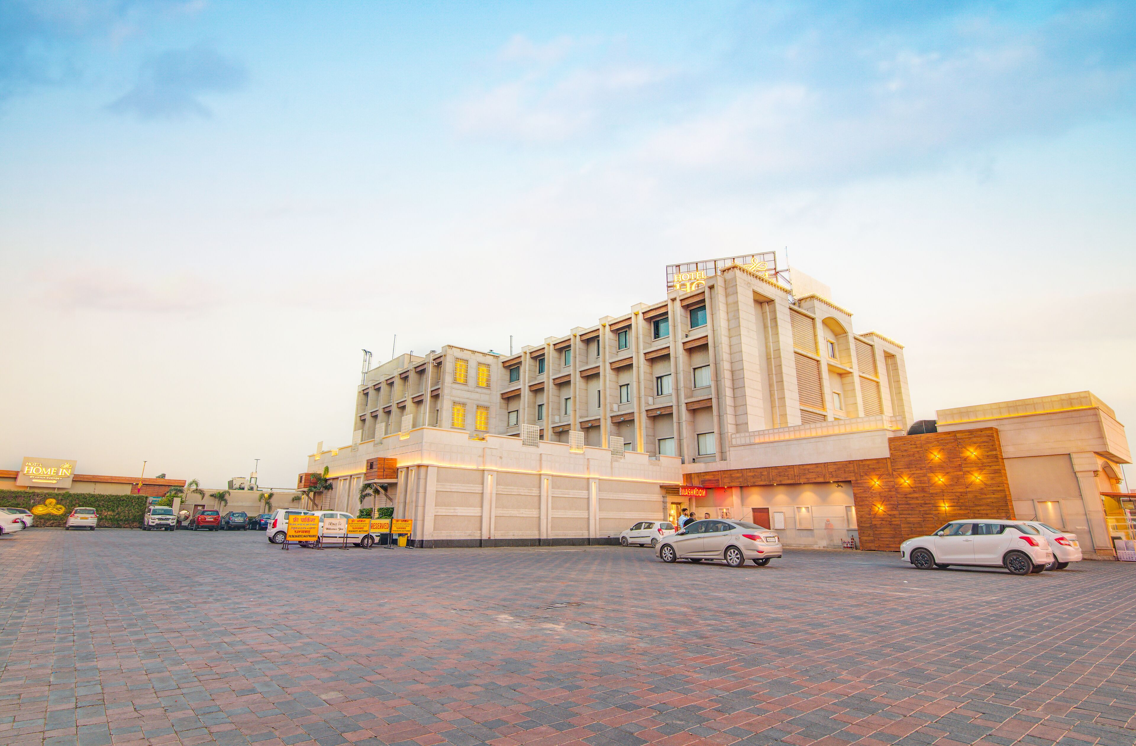 Um hotel com fachada moderna, vários andares e um estacionamento com diversos carros.