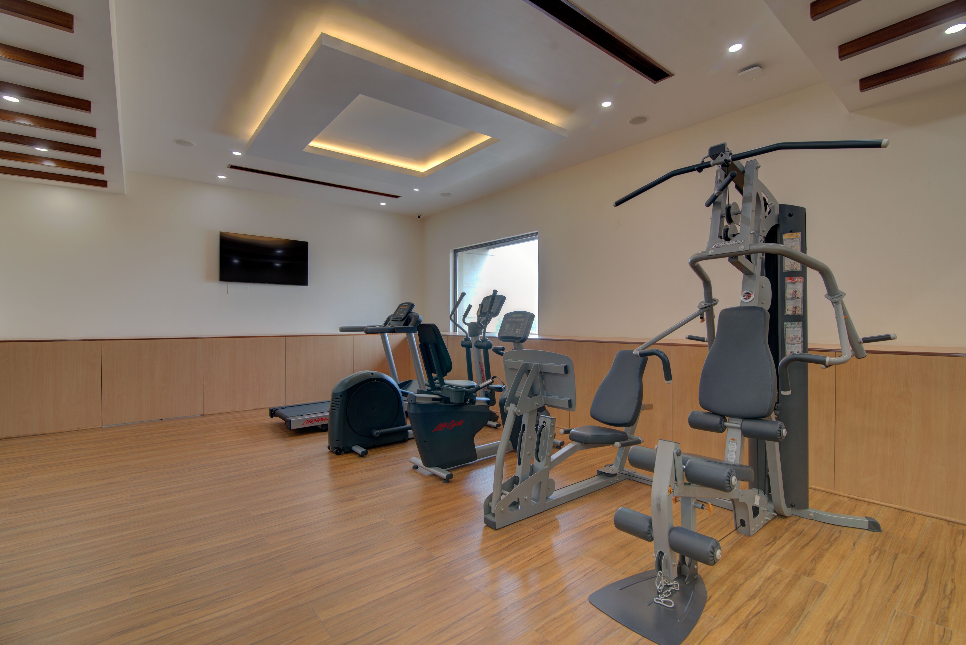 A gym with exercise equipment, a television, and a window.