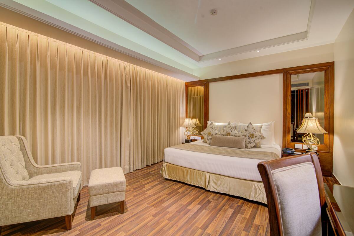 A hotel room with a large bed, two chairs, a small table, and a mirror.