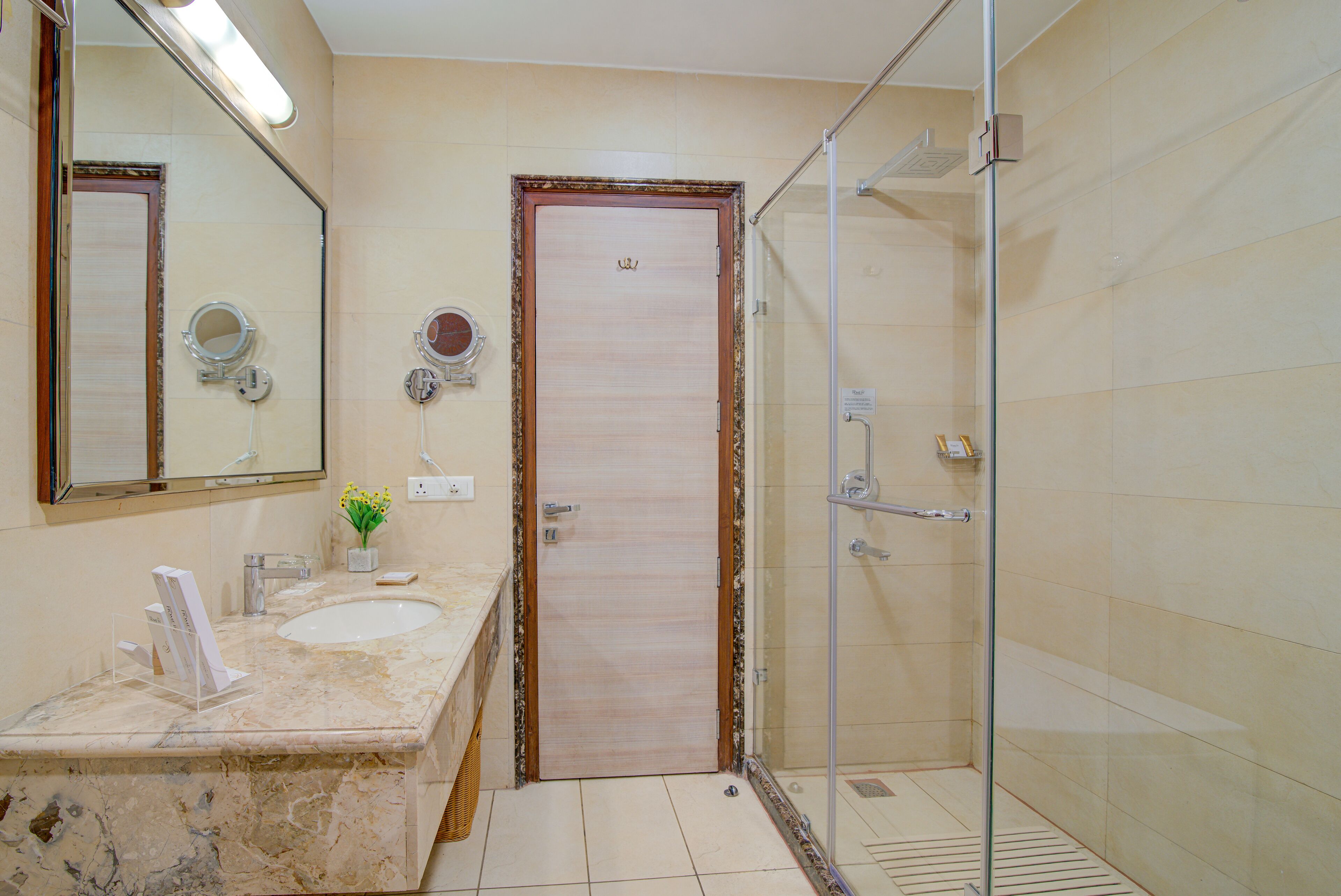 A bathroom with a marble sink, a mirror, a shower, and a door.