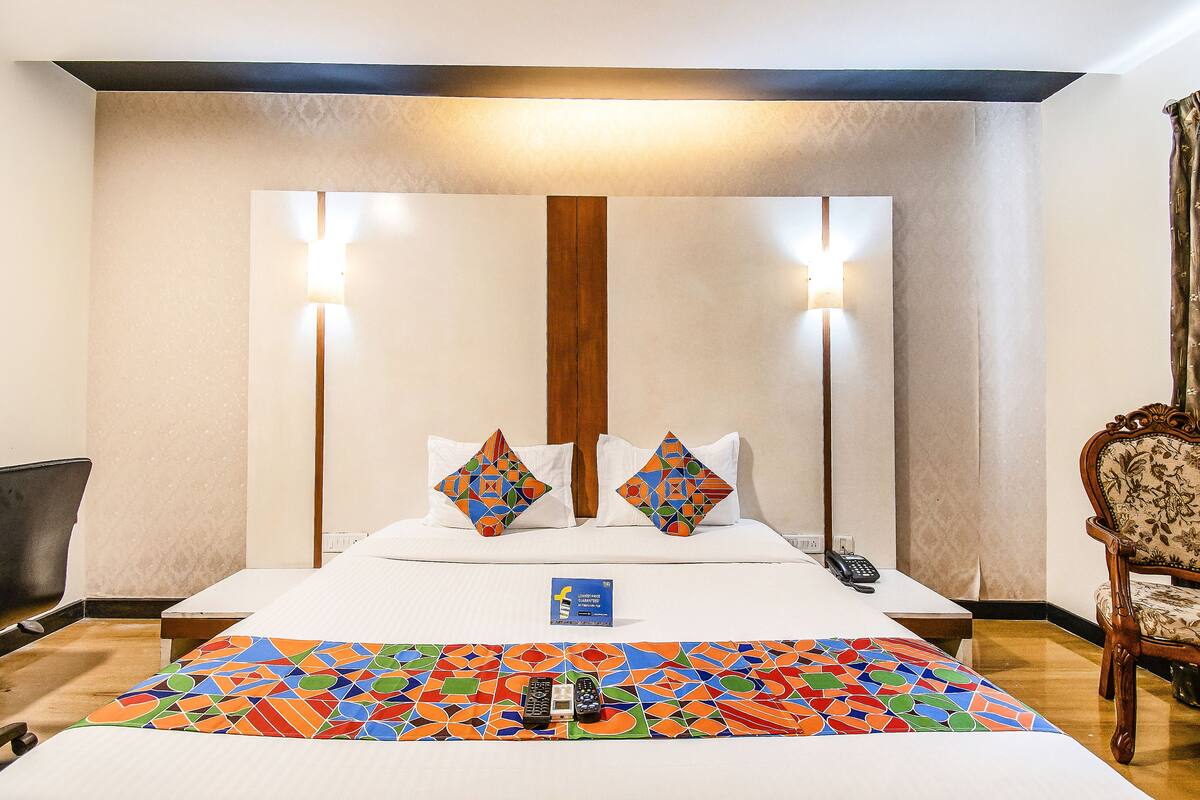 A hotel room with a bed, two decorative pillows, a bedside table with a phone, a chair, and a colorful rug.