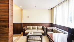 A living room with a brown leather sofa, a wooden coffee table, and a view of a cityscape through large windows. - FabHotel Oriental Suites MG Road (Bengaluru)