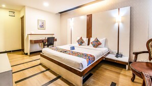 A hotel room with a large bed, bedside table, desk, and chair. - FabHotel Oriental Suites MG Road (Bengaluru)