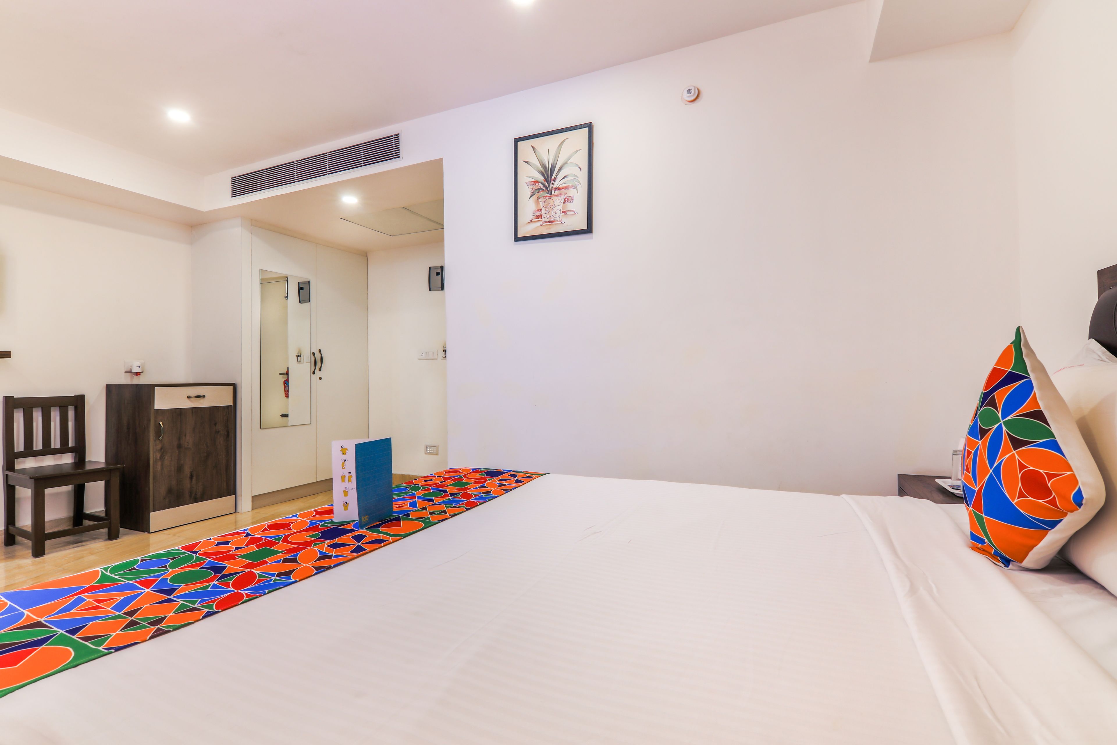 Una habitación de hotel con cama, escritorio, silla, armario y una alfombra colorida.