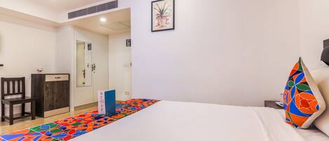 Una habitación de hotel con cama, escritorio, silla, armario y una alfombra colorida.
