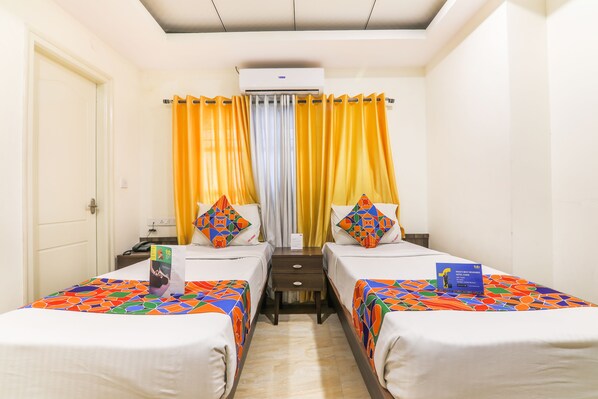 Quarto de hotel com duas camas, uma mesinha de cabeceira, um ar condicionado e uma cortina.
