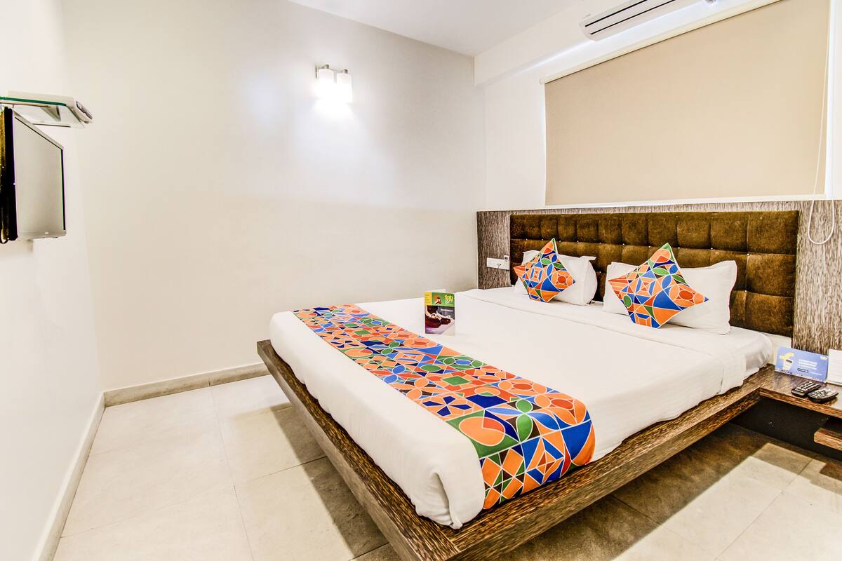 A neatly made bed with a colorful geometric-patterned bedspread and matching pillows, a wooden headboard, and a bedside table with a remote control.