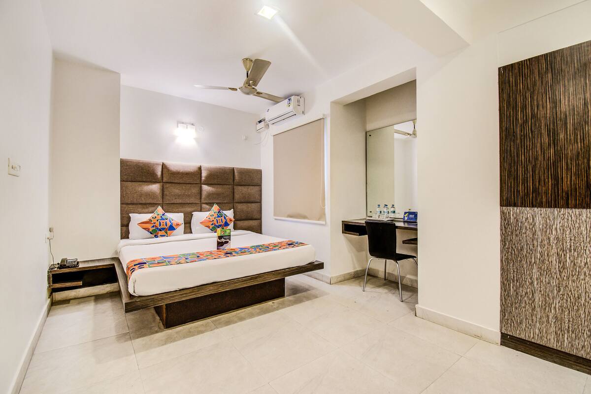 A modern hotel room with a large bed, a desk, and a ceiling fan.