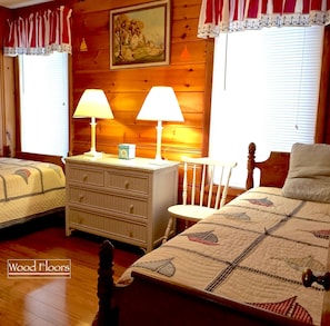 Quarto com duas camas de solteiro, ar condicionado central e ventoinha no teto, e piso de madeira.