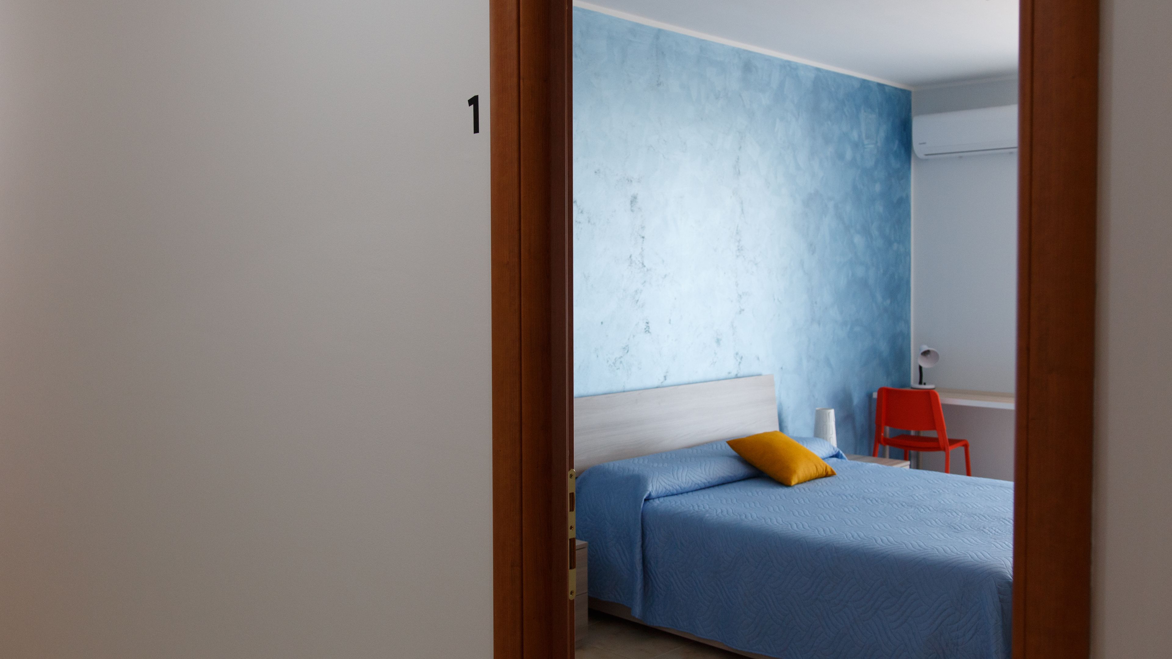 A bedroom with a bed, a red chair, and a wall with a textured design.