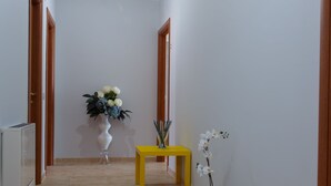 A hallway with a tiled floor, a white vase with flowers, a yellow table, and a potted plant. - B&B Mediterraneo (Floridia)