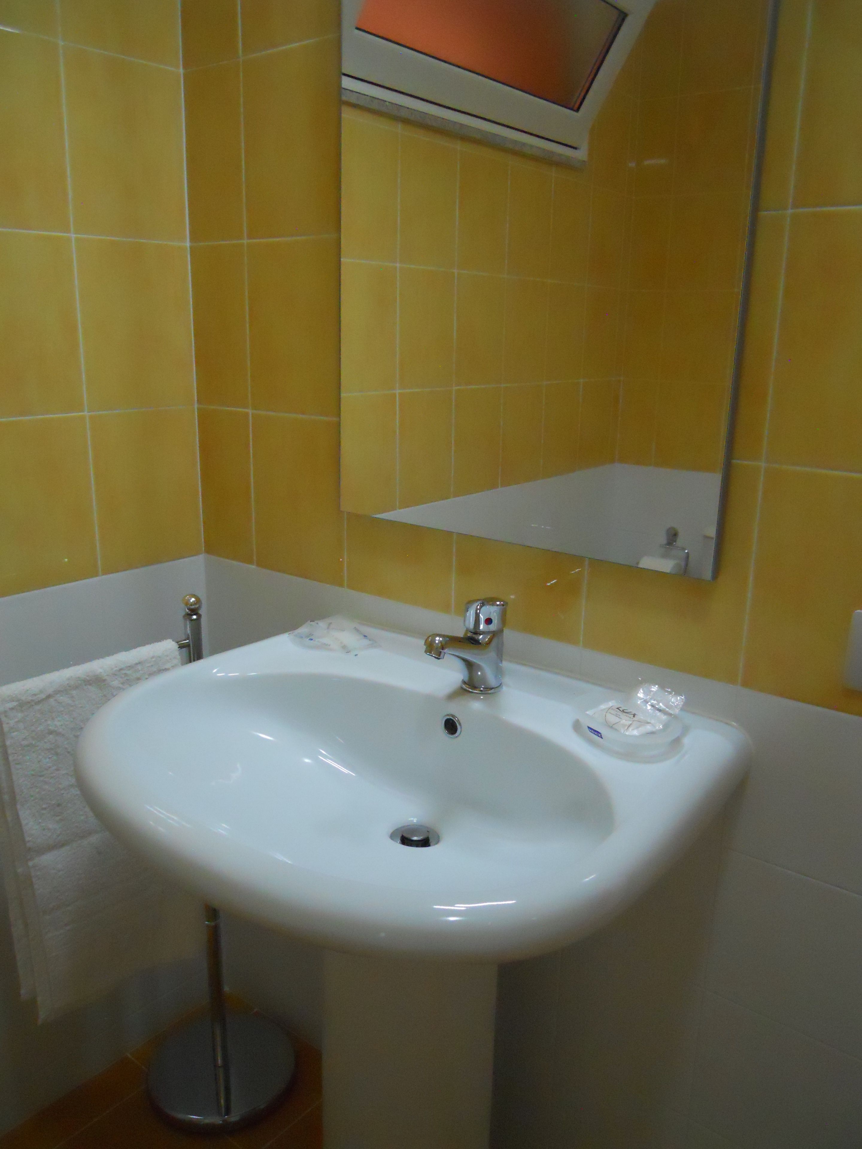 Un baño con lavamanos blanco, azulejos amarillos, un espejo y un perchero para toallas.