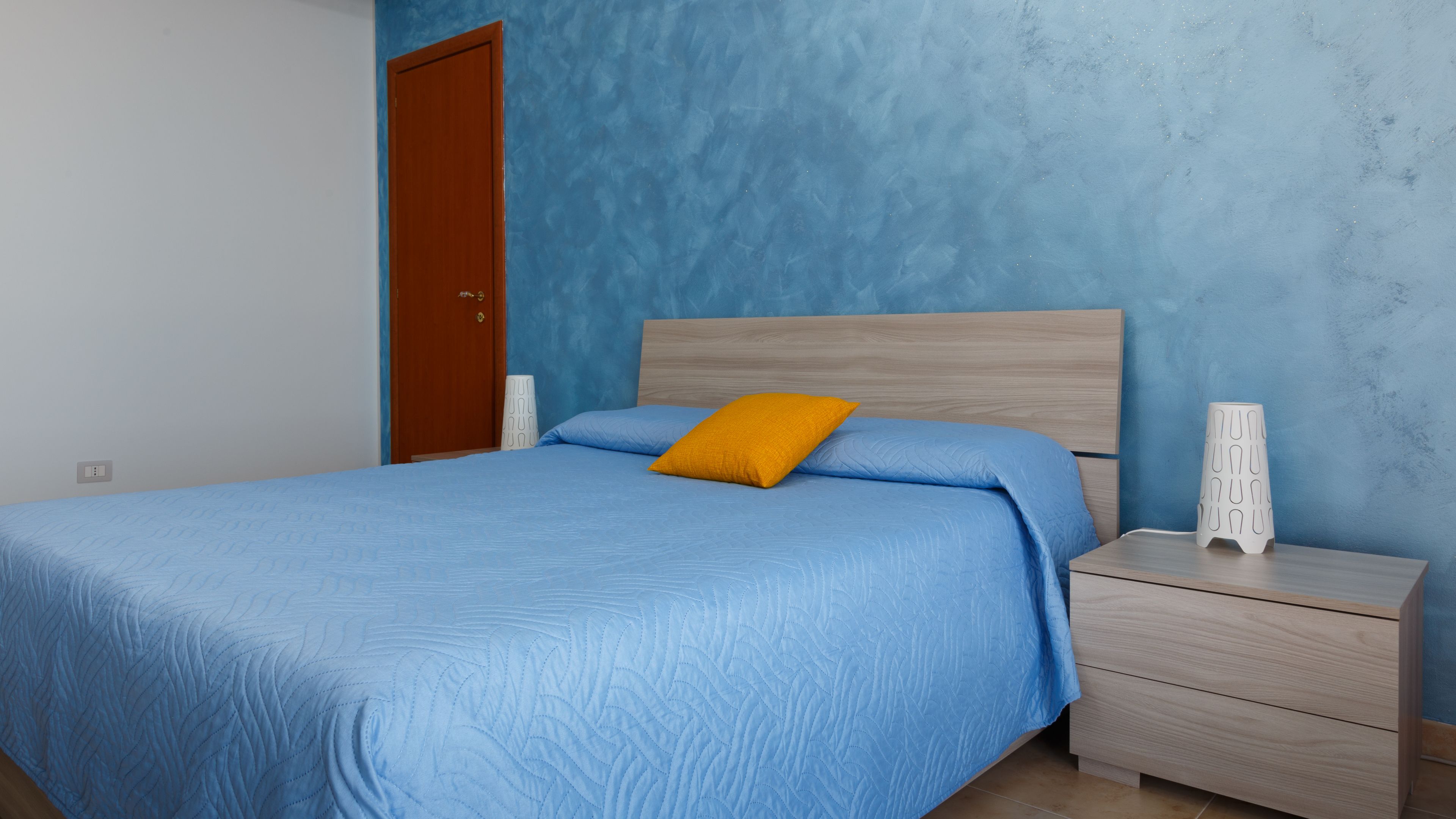 Una camera da letto con un letto, una testiera in legno, un comodino e una lampada bianca.