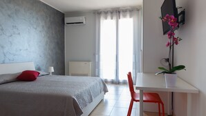 A bedroom with a bed, a desk, a chair, a potted plant, and a window with curtains. - B&B Mediterraneo (Floridia)