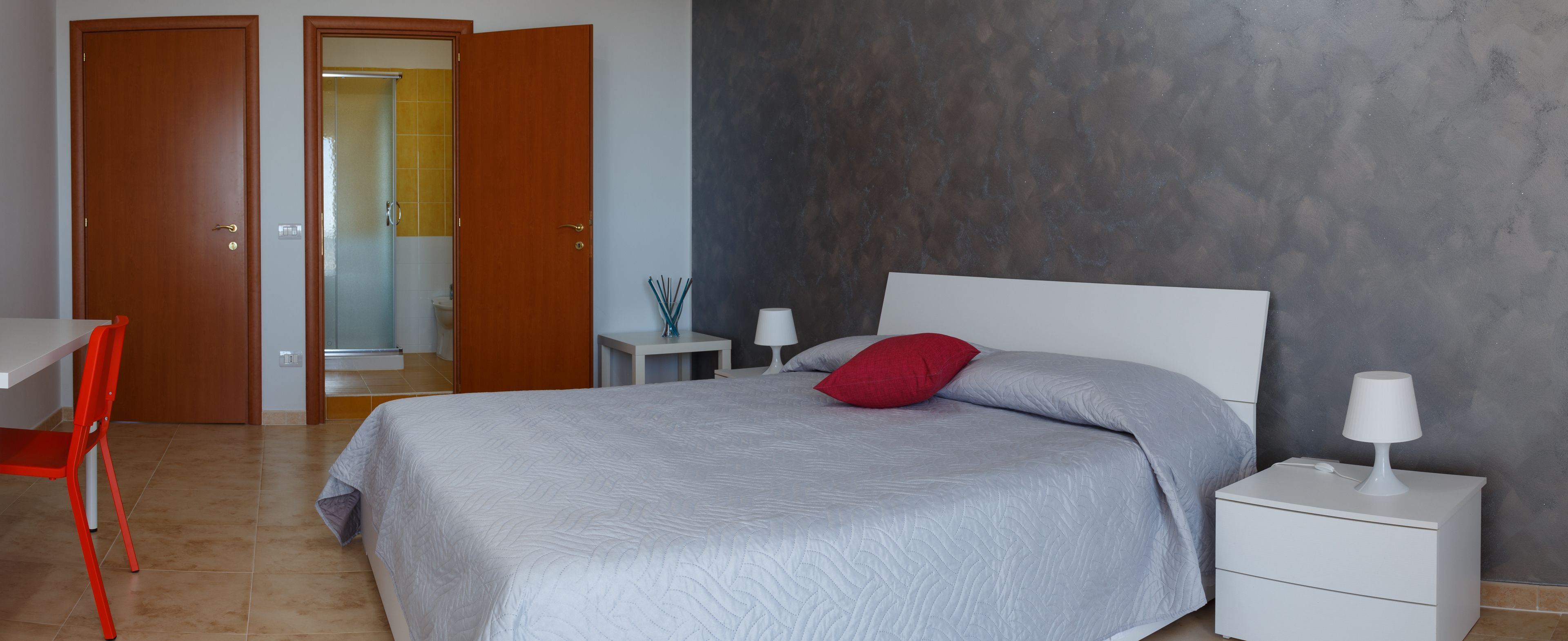 A bedroom with a bed, a nightstand, a desk, and a chair.