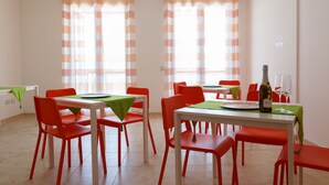 A dining area with red chairs and a white table, a bottle of wine, and a glass on the table. - B&B Mediterraneo (Floridia)