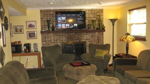 Una sala de estar con chimenea de ladrillo, un televisor montado encima y una mesa de centro con un control remoto.