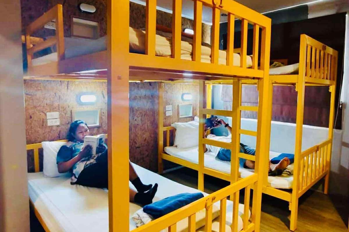 A dormitory room with bunk beds, wooden flooring, and a brick wall.