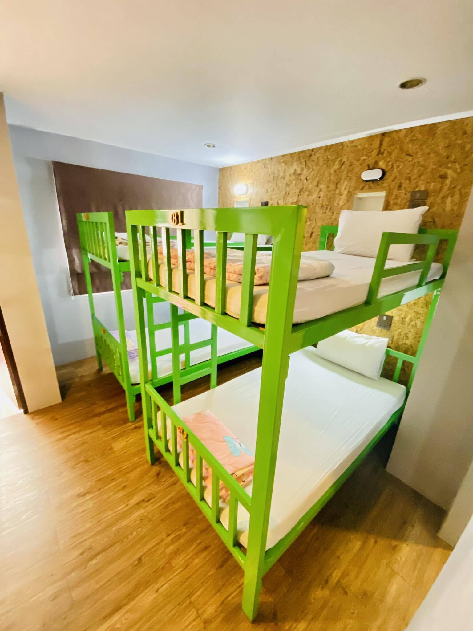 A bunk bed room with a wooden floor, a wall-mounted light, and a window.