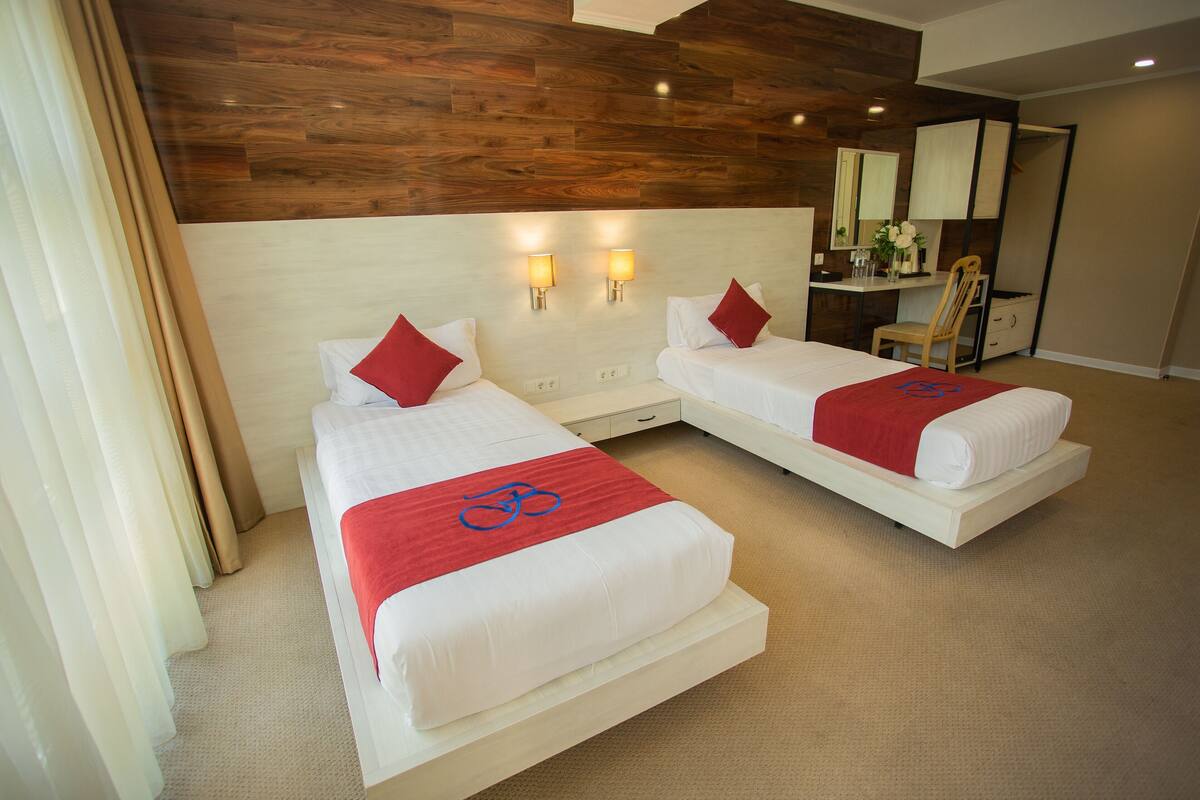Ein Hotelzimmer mit zwei Betten, einer Holzbalkendecke, einem Schreibtisch mit Stuhl und einem Spiegel.