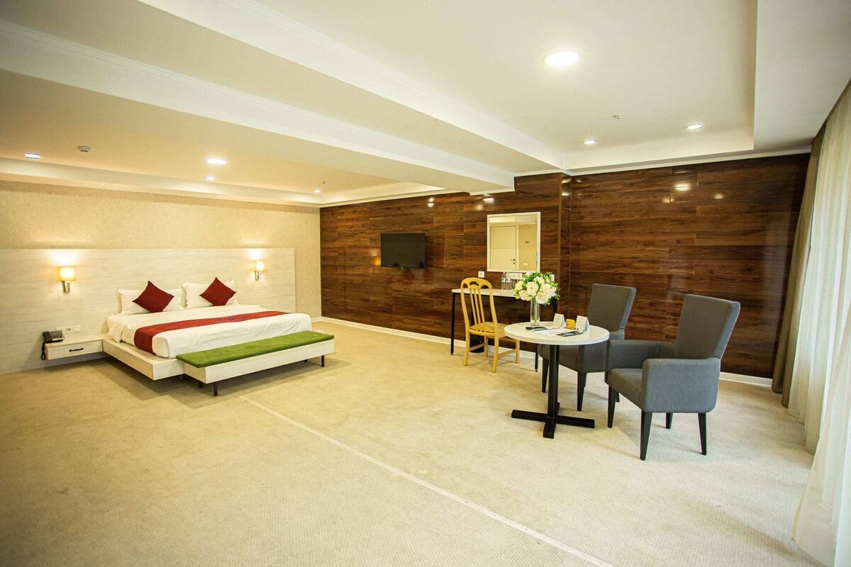 Ein modernes Hotelzimmer mit Bett, Nachttischen, einem Schreibtisch mit Stuhl, einem Spiegel und einer Wand mit Holzverkleidung.