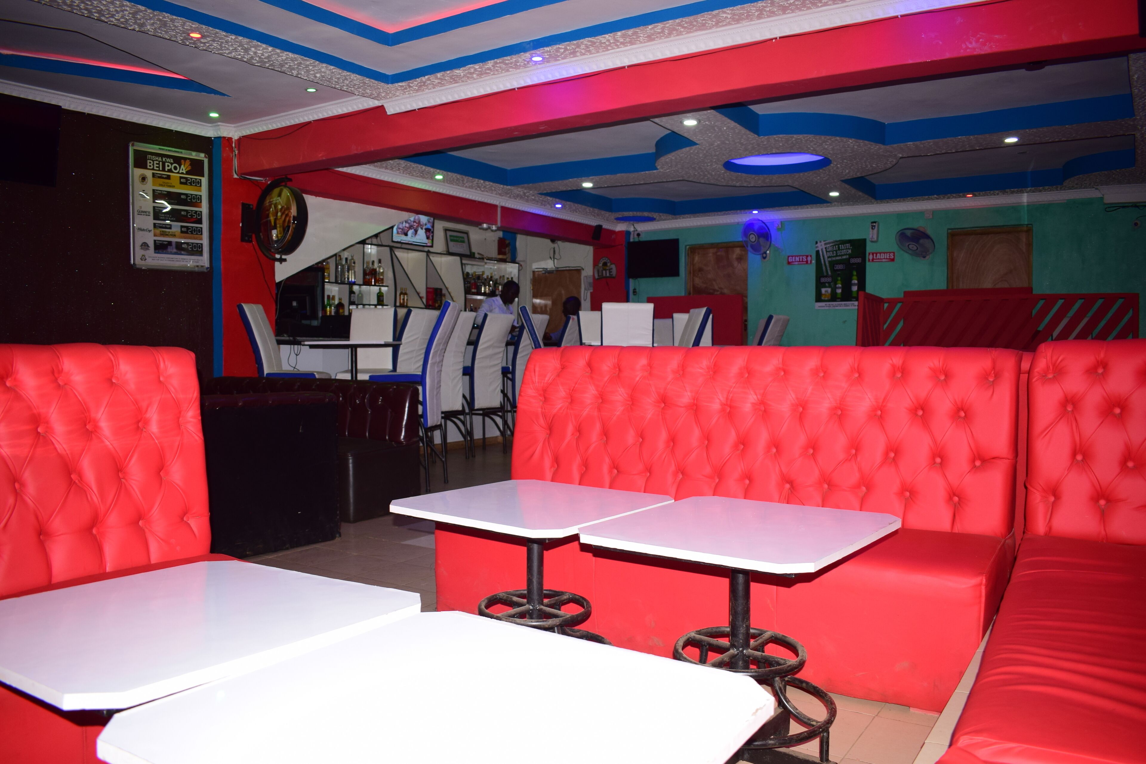 A restaurant with red upholstered booths and white tables, a bar area, and a ceiling with blue and white patterns.