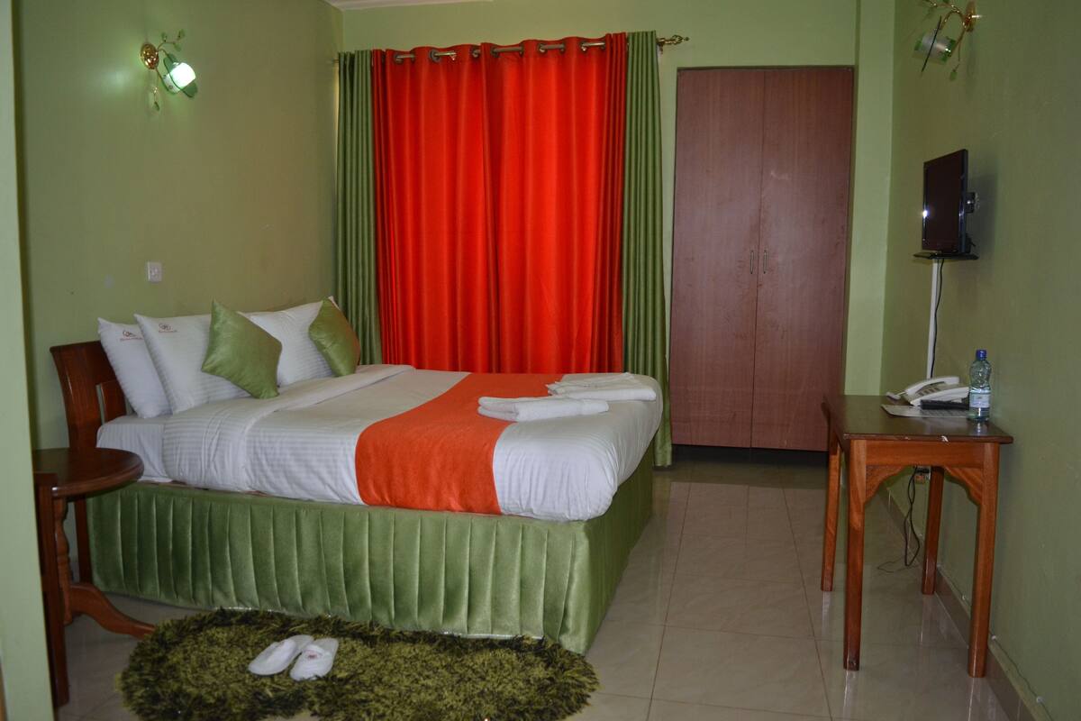 Una habitación de hotel con una cama, una mesita de noche de madera, una alfombra verde y una cortina roja.