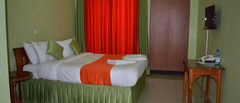 Una camera d'albergo con un letto, un comodino in legno, un tappeto verde e una tenda rossa.