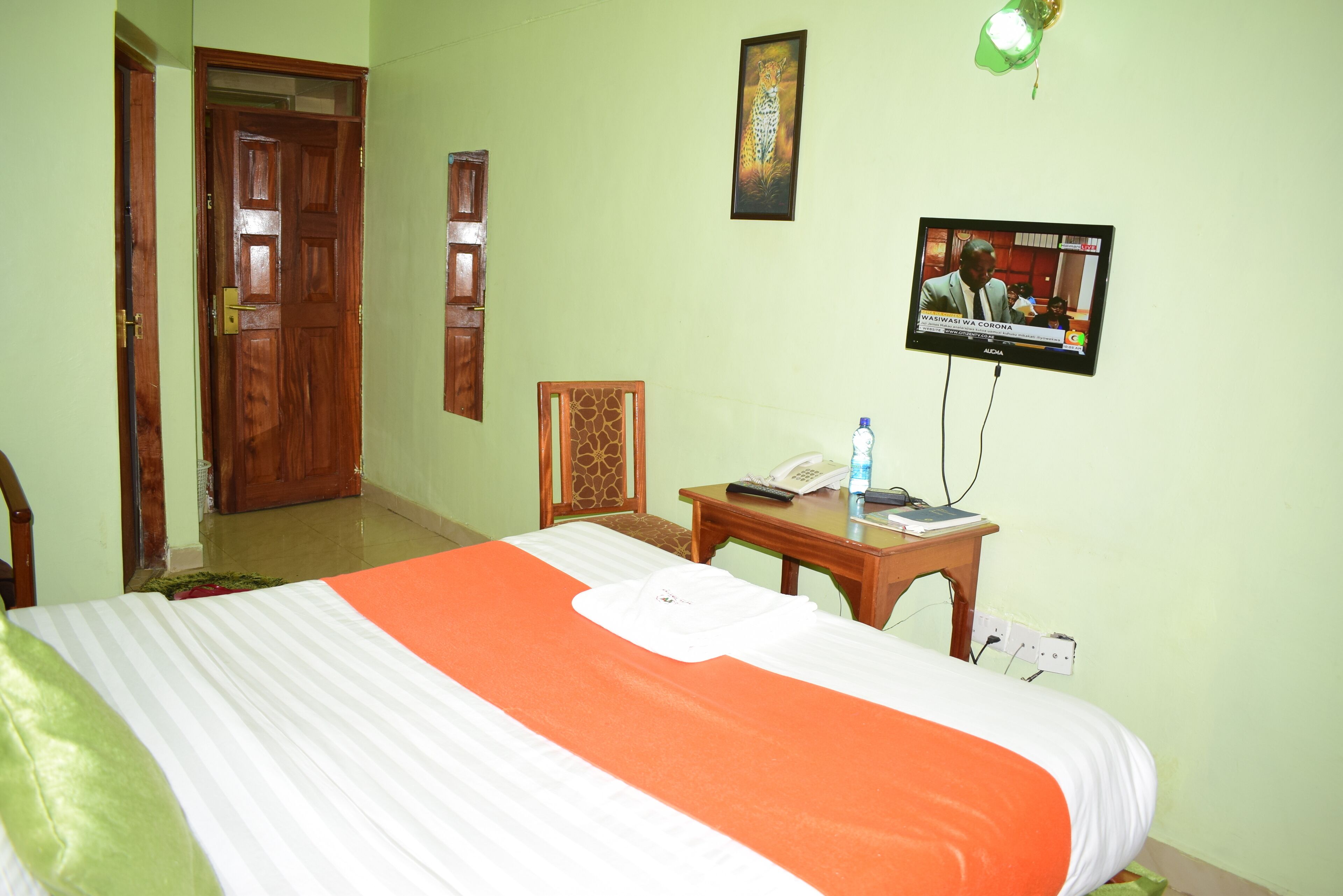 A hotel room with a bed, a television, a desk with a phone, and a door.