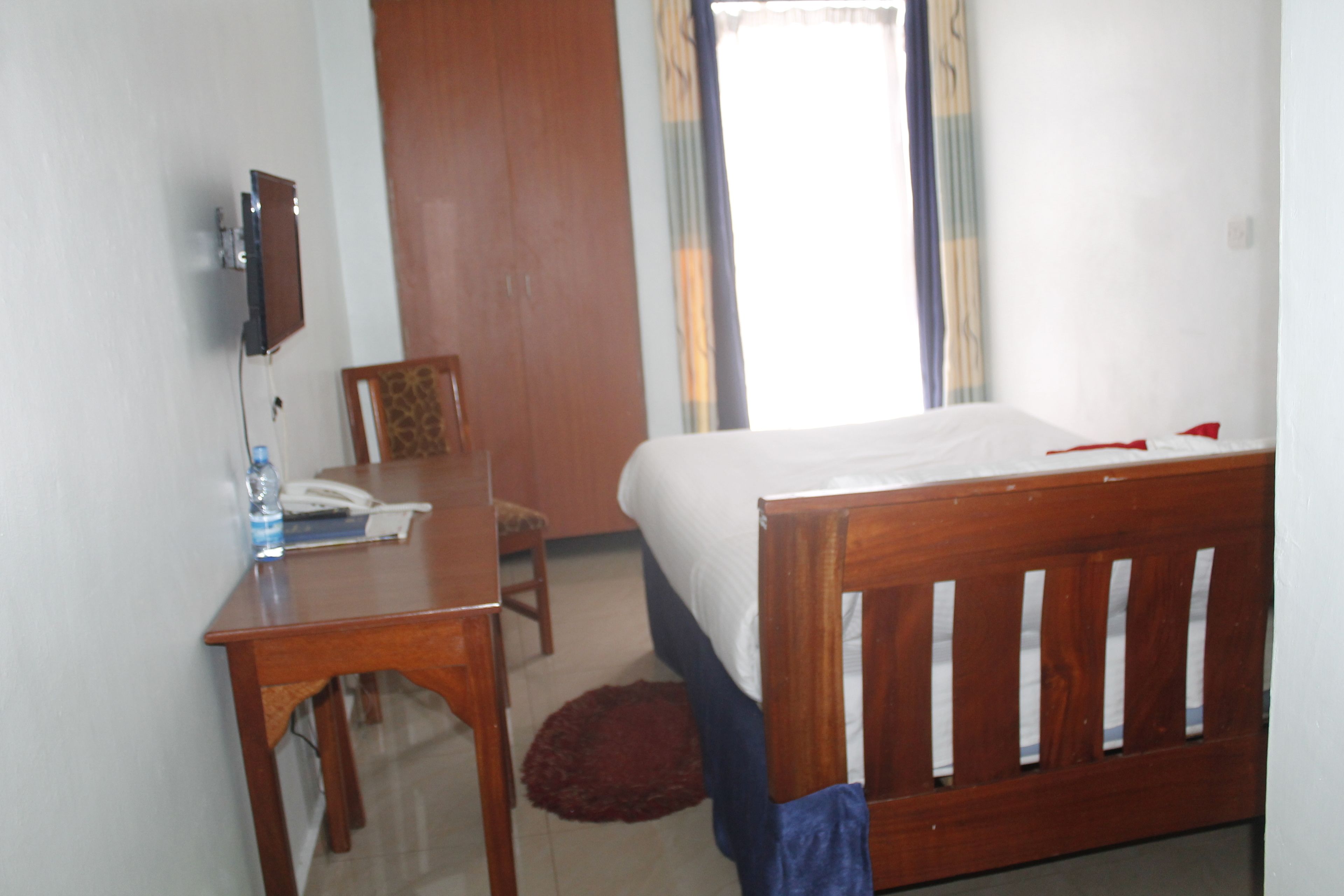 Un dormitorio con una cama de madera, un escritorio con una silla, un teléfono y un televisor montado en la pared.