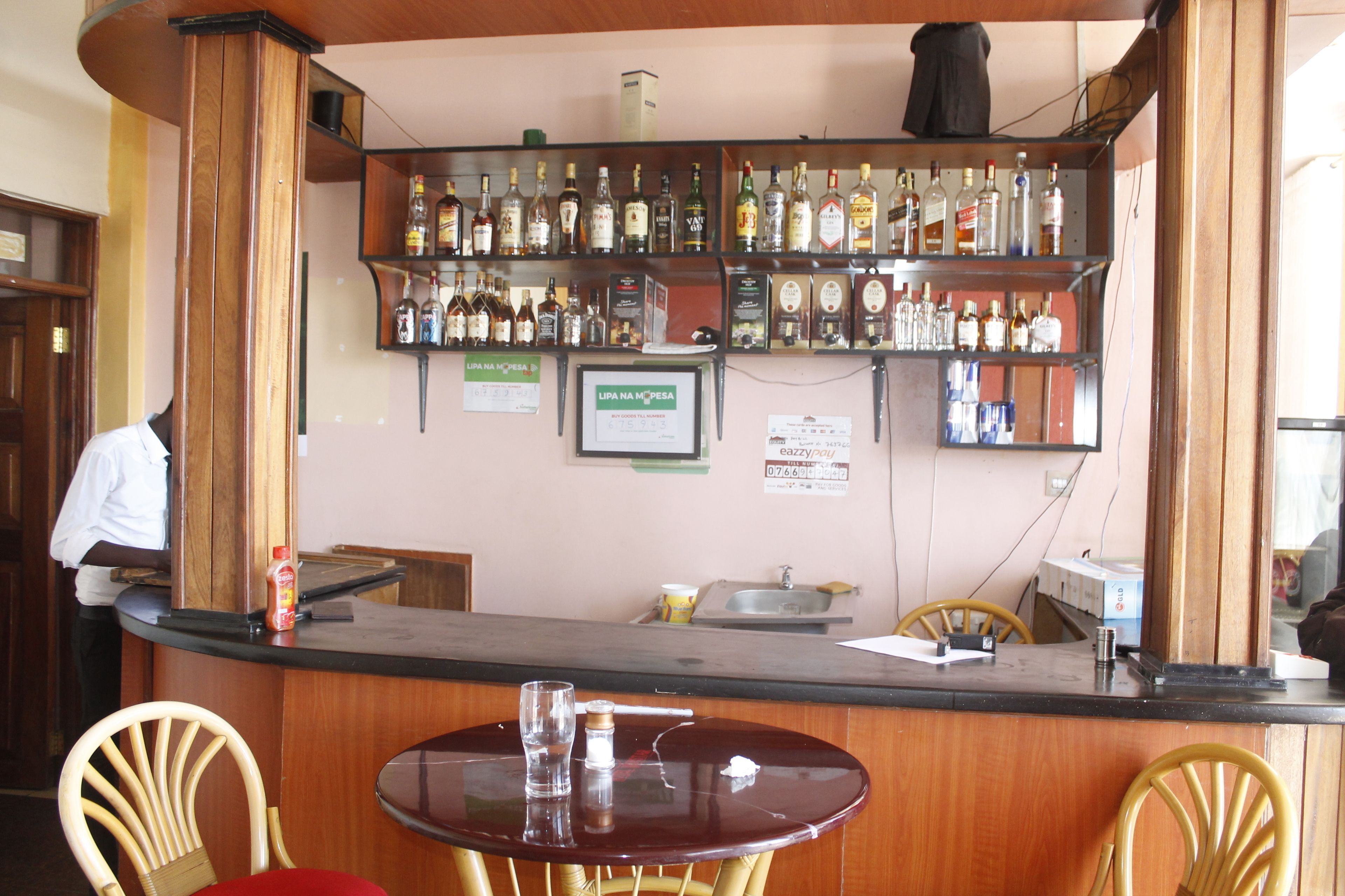 A bar area with wooden furniture, a counter with various bottles, and a sign on the wall.