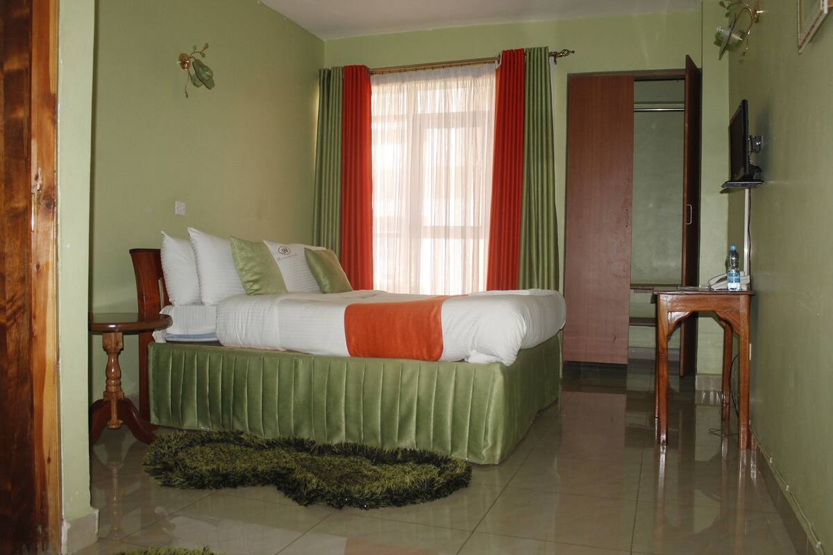 Un dormitorio con cama, mesita de noche, espejo y ventana con cortinas.