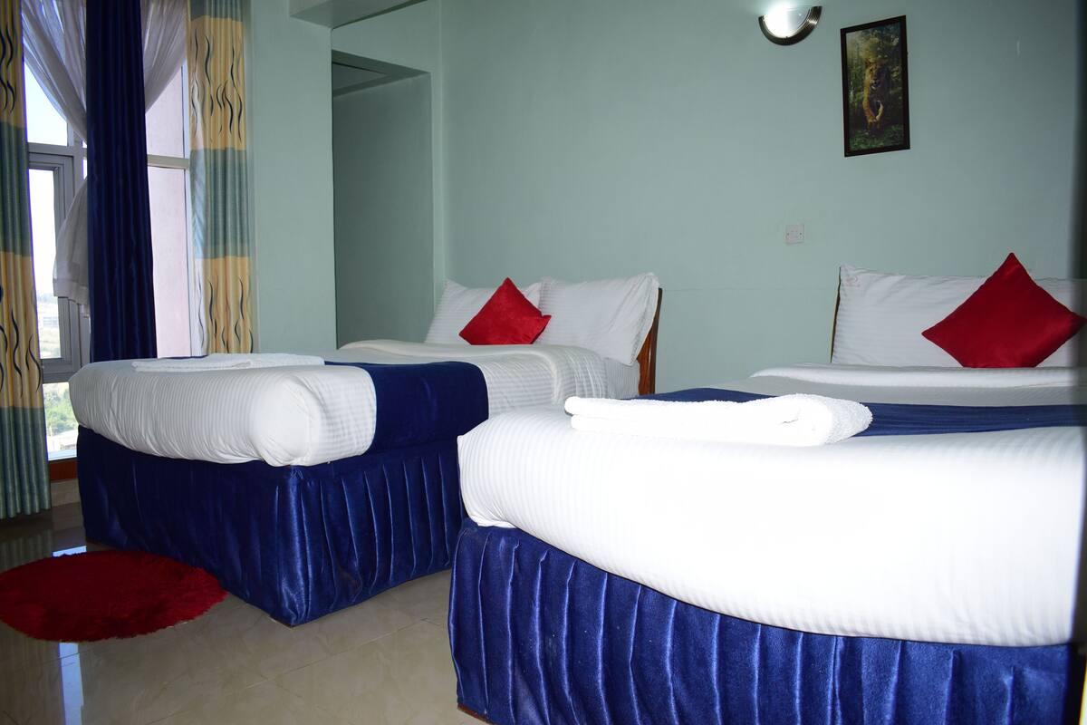 Habitación de hotel con dos camas, cada una con ropa blanca y almohadas rojas, y una alfombra roja en el suelo.