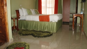 Una habitación de hotel con una cama, una mesita de noche de madera, una alfombra verde y una pequeña mesa de madera.