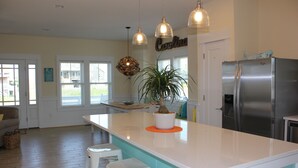 A kitchen with a central island, stainless steel refrigerator, pendant lights, and a potted plant.