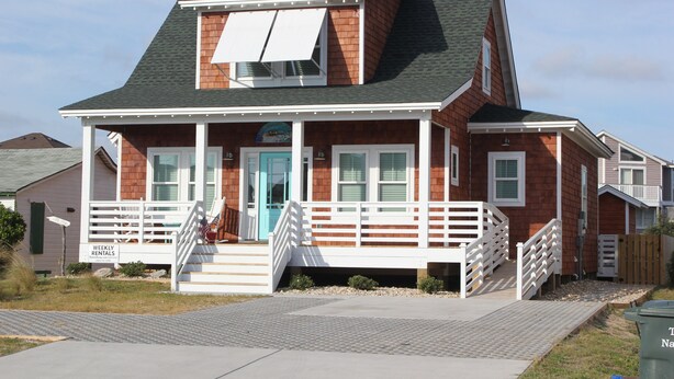 A two-story house with a front porch, a blue door, and a staircase leading to the entrance.