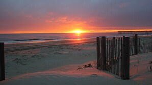 A beach with a wooden fence and a sunset in the background.
