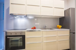 Une cuisine équipée d’un four encastré, d’un réfrigérateur en acier inoxydable et d’un saladier rempli de fruits posé sur le plan de travail.