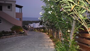 Un vialetto lastricato conduce a un edificio con facciata in pietra, circondato da vegetazione e con vista sul mare.