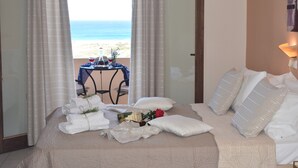 Una camera d'albergo con un letto, cuscini bianchi, un bouquet di fiori e vista sulla spiaggia.