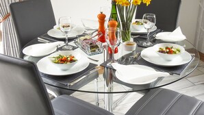 Ein Esstisch mit weißen Tellern, klarem Glas und einem Blumenarrangement aus gelben Blüten.