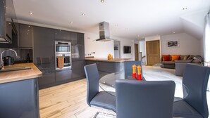 Eine moderne Küche mit Kochinsel, ein Essbereich mit Glastisch und ein Wohnzimmer mit Sofa und Fernseher.