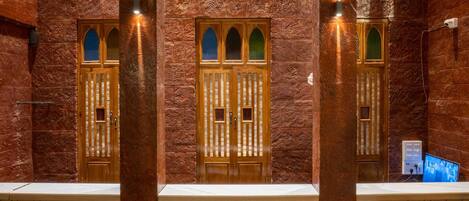 A lobby with a herringbone patterned floor, wooden doors with arched windows, and decorative wall panels.