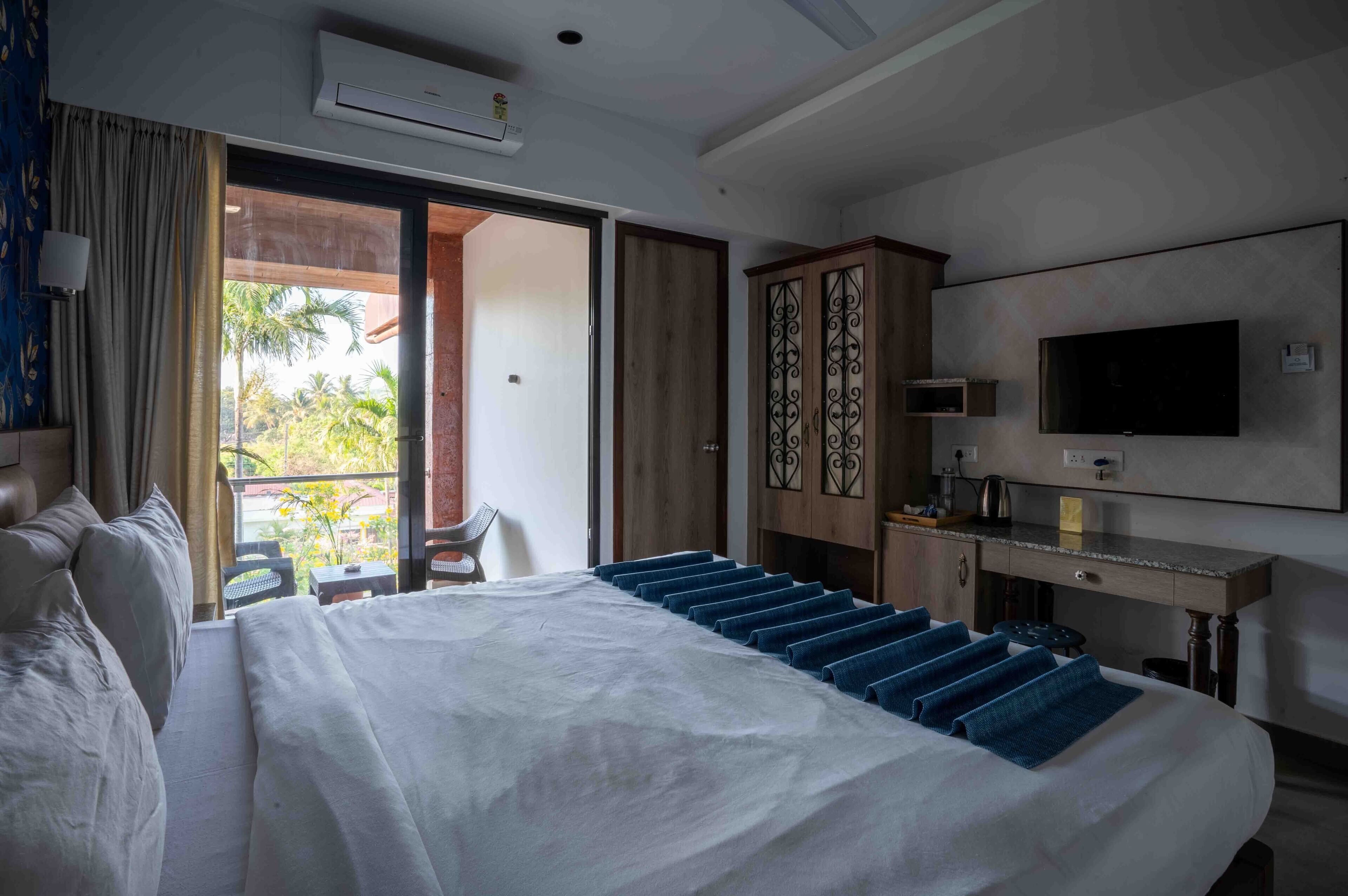 Camera d'albergo con un letto grande, televisione, scrivania e balcone con vista sulle palme.