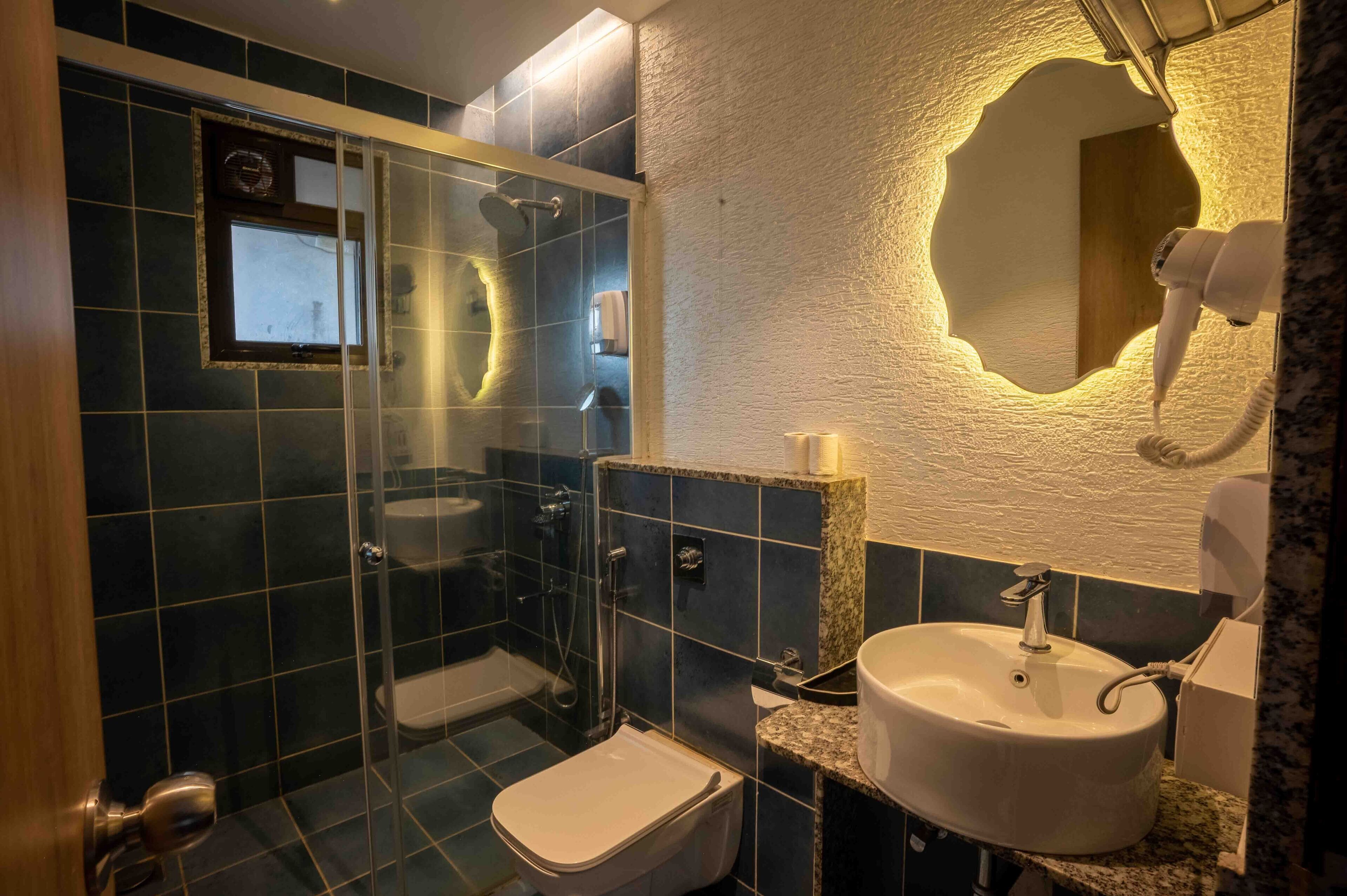 Une salle de bain dotée d’une douche à parois de verre, de toilettes, d’un lavabo et d’un miroir dont le design présente un orifice original.