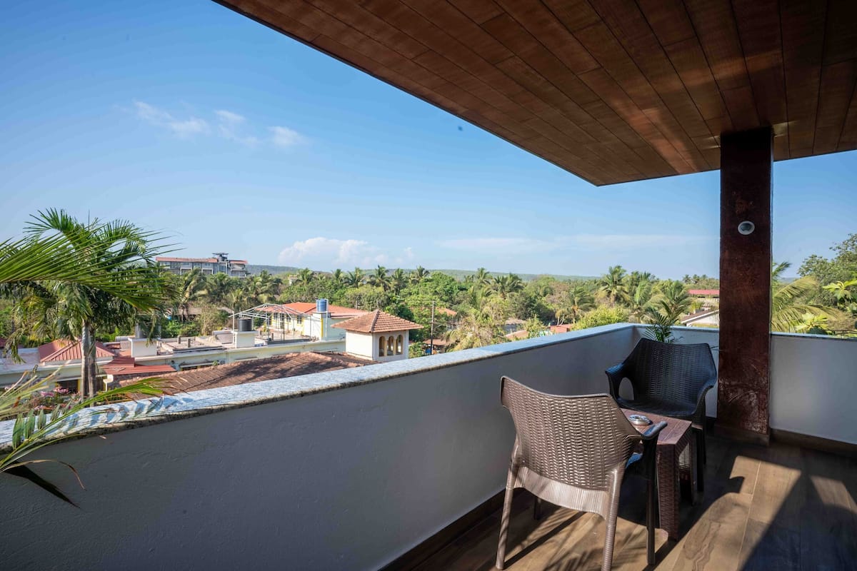 A balcony with wicker furniture, a view of a residential area, and a clear sky.