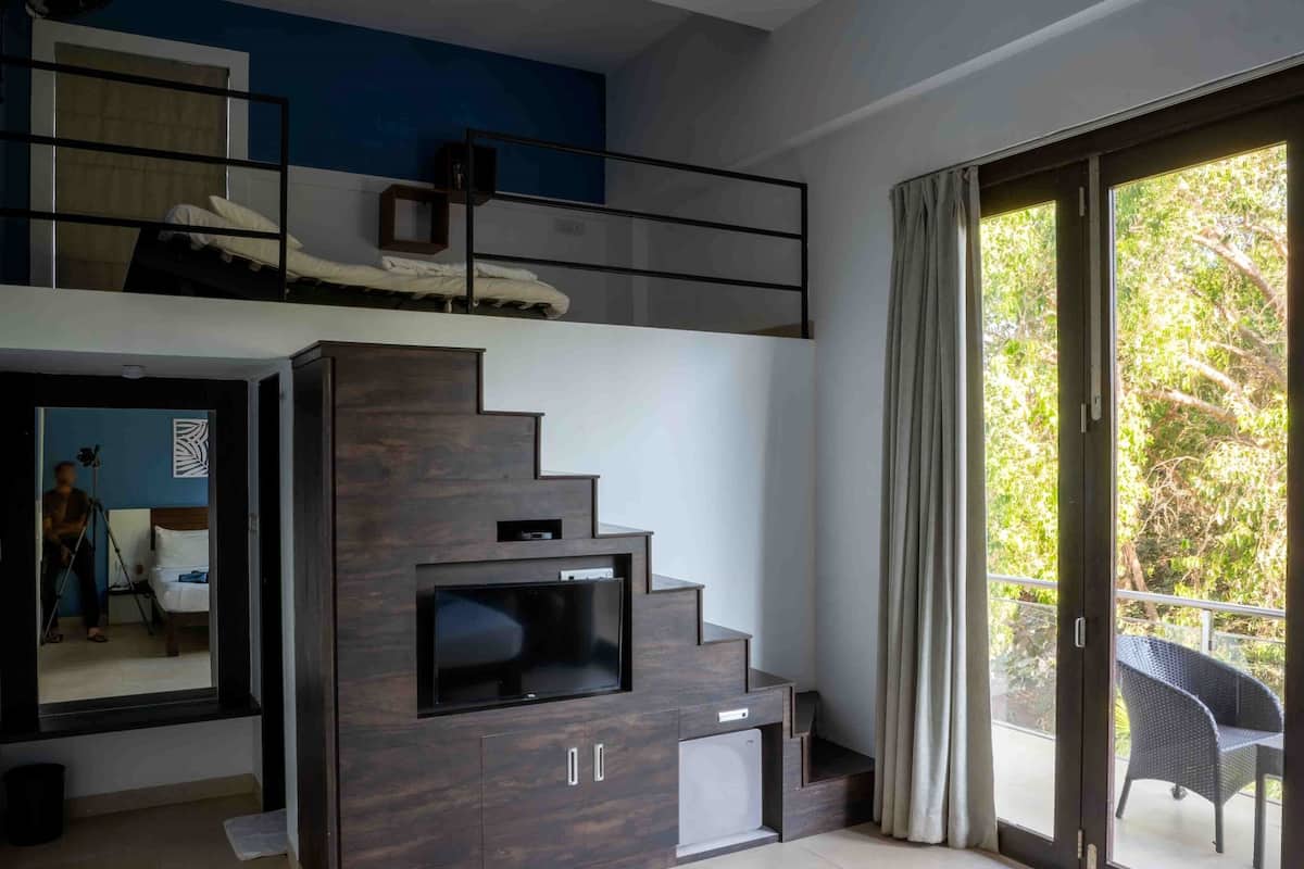 A modern hotel room with a bed, a TV, a balcony with a chair, and a staircase leading to an upper level.
